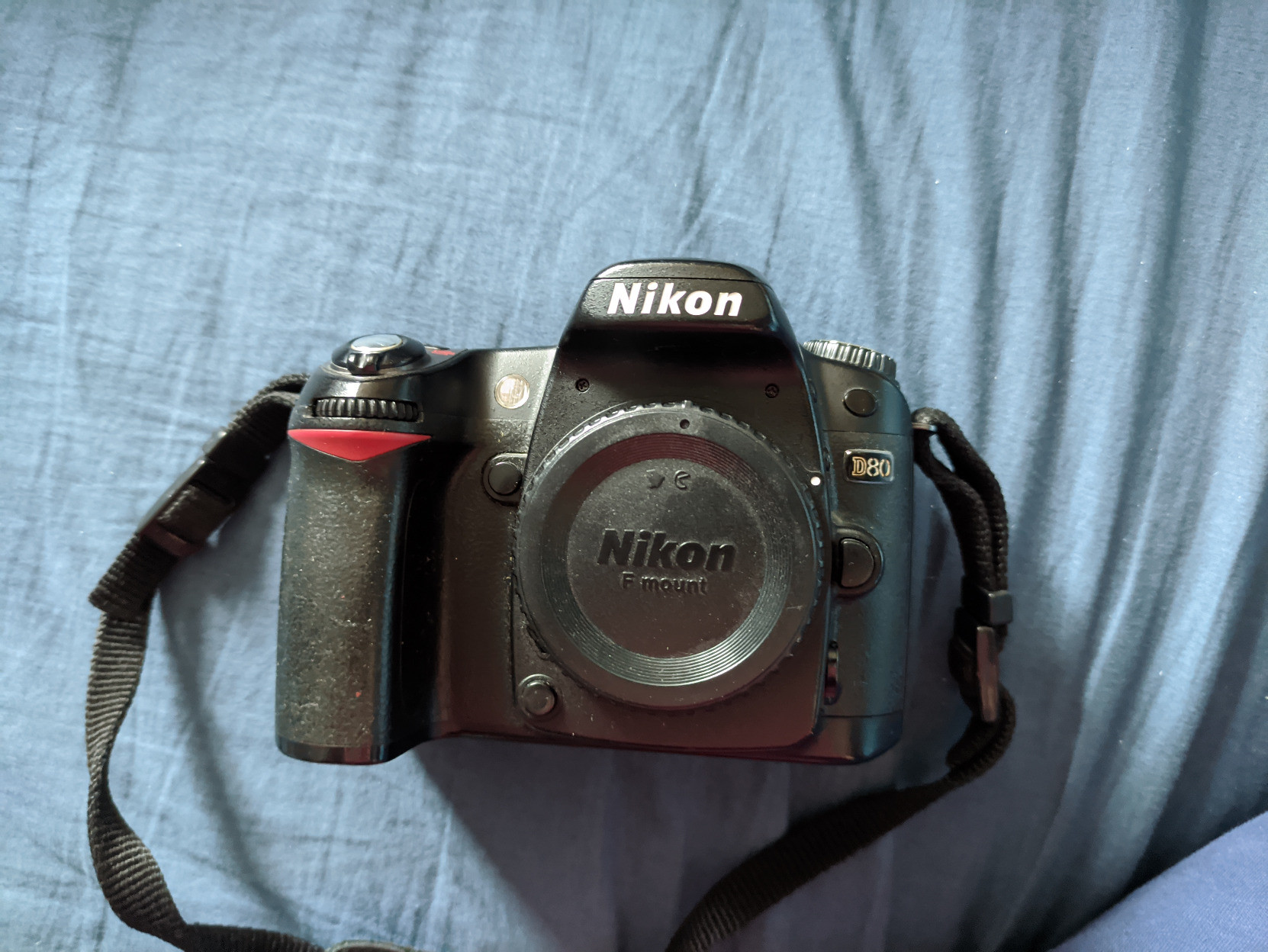 A photo of the front of the Nikon D80 DSLR. There is no lens attached, only a protective cover.