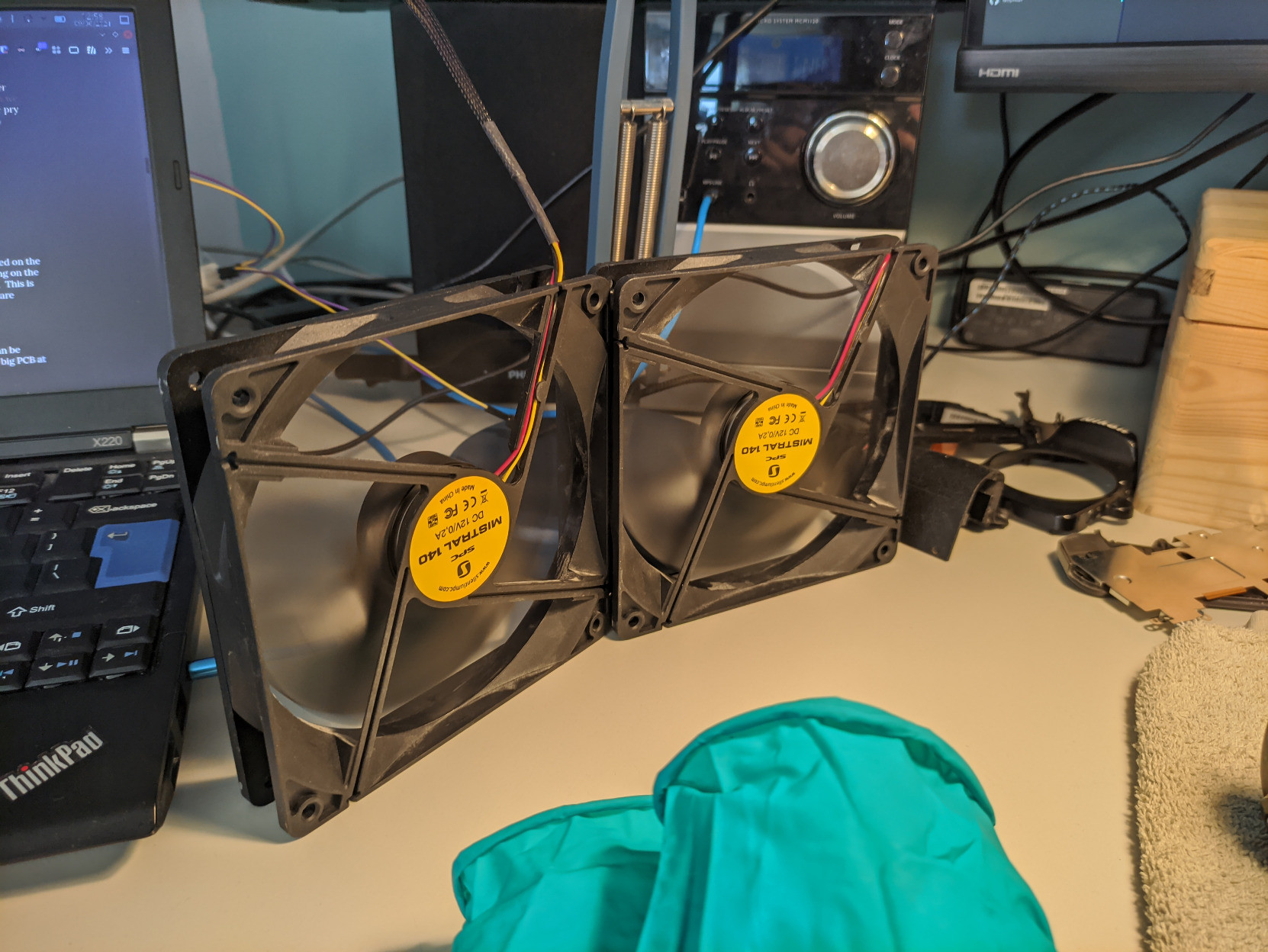 A picture of two black 120mm computer fans on the left side of my desk.