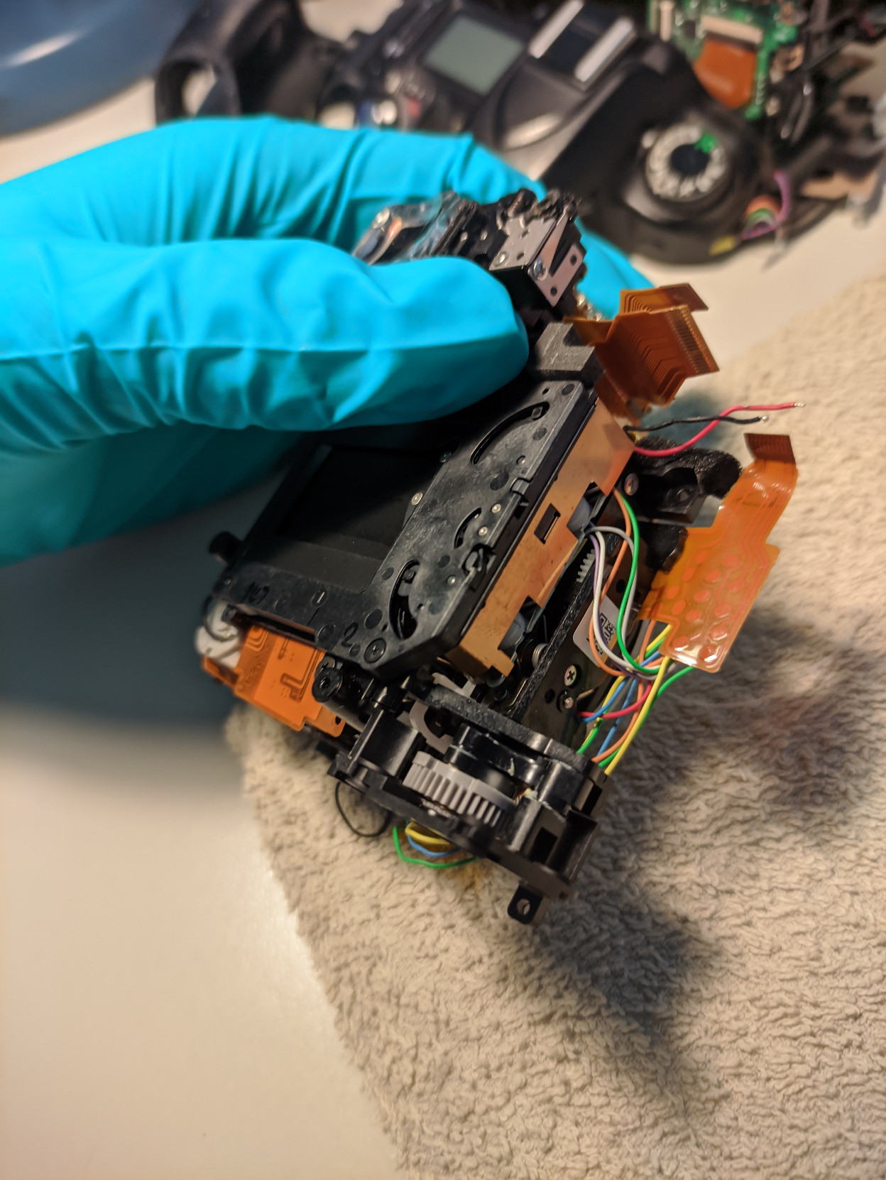 A photo of the front internal assembly with the aperture control unit taken out. You can see that under where it was there is a plastic gear, which is the broken part.